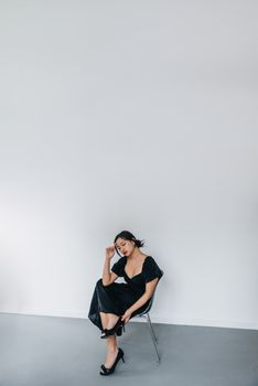 Asian woman posed gracefully in a studio setting wearing a classic black dress with high heels.