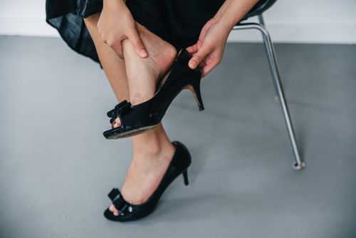 Free Close-up of a woman removing black high heels while seated indoors. Stock Photo