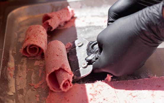 Close-up of hands preparing delicious rolled ice cream on metal tray.