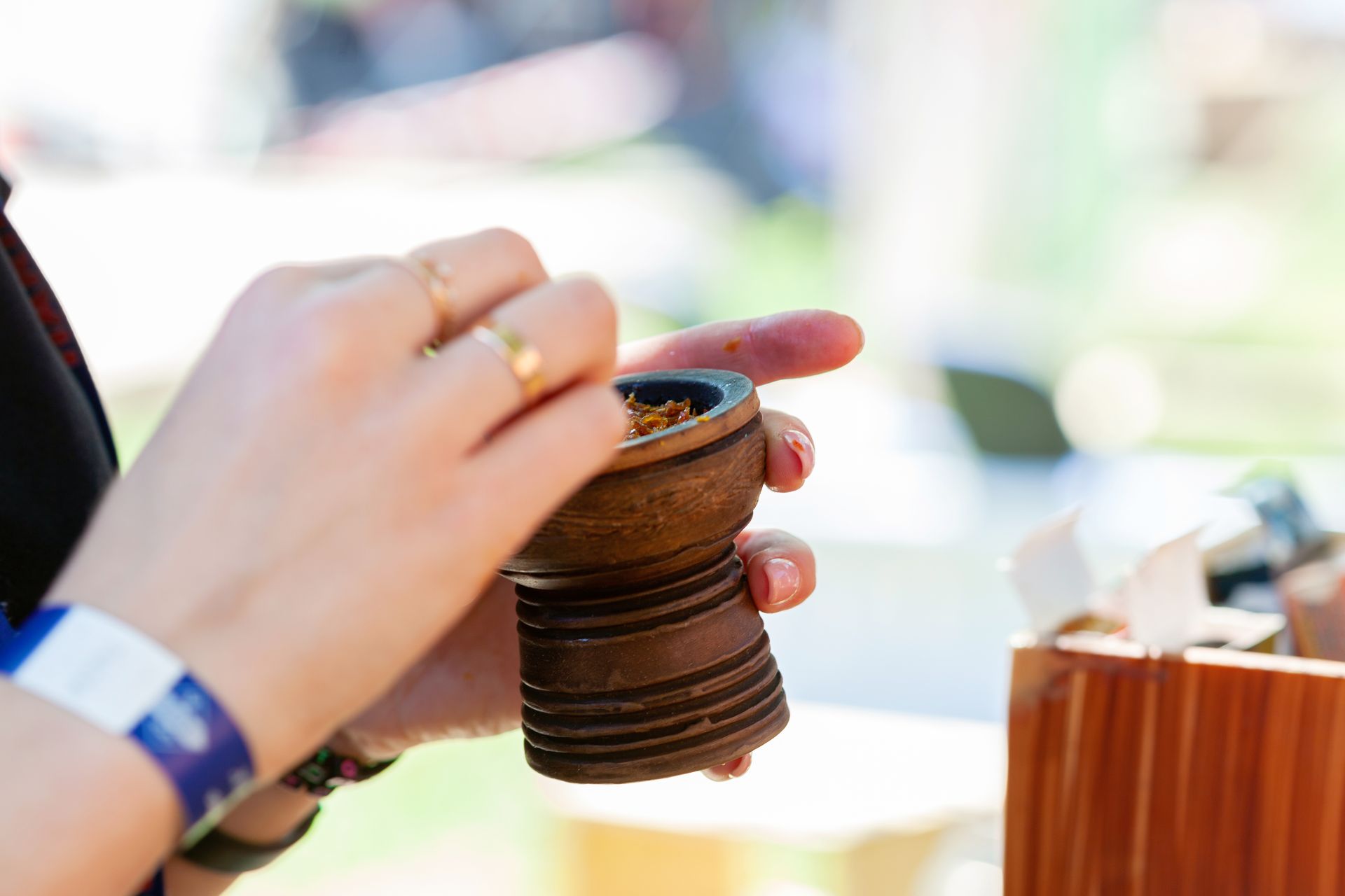 Close-up of a person stirring tobacco in a bowl outdoors, showing hands and accessories.