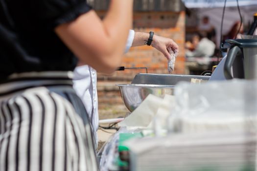 Chef frying food in an outdoor kitchen setting, showcasing hand and utensil focus.
