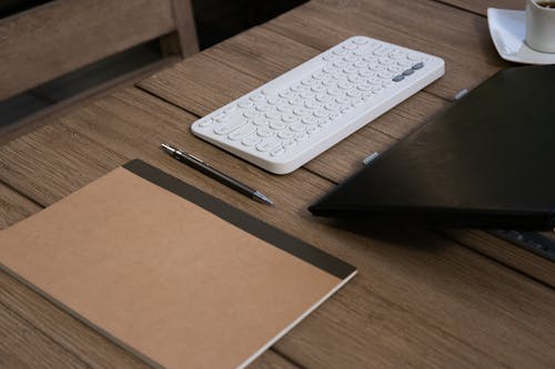 A Notebook Near a White Keyboard