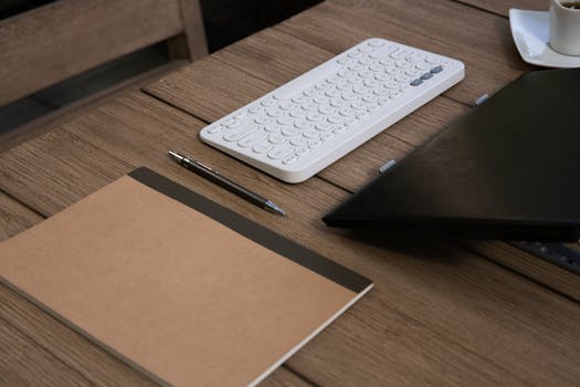 Minimalist office setup featuring keyboard, notebook, and pen on a wooden desk.