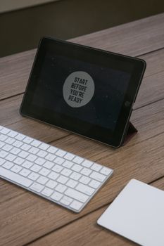 A tablet displaying an inspirational quote next to a keyboard on a wooden desk.