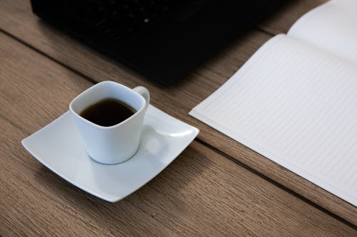 Free Ceramic Cup and Saucer Next to an Open Notebook  Stock Photo