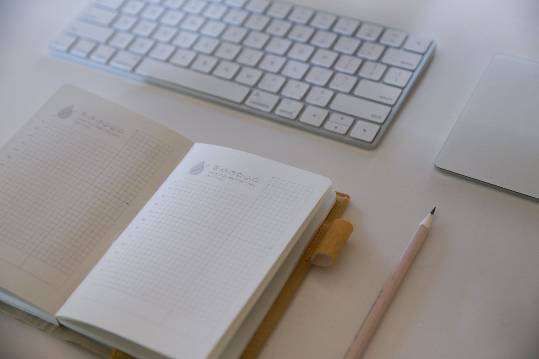 A clean and simple workspace featuring a keyboard, notebook, and pencil.