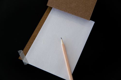 Free Elegant flat lay of a pencil on white paper with a brown cardboard on black background. Stock Photo