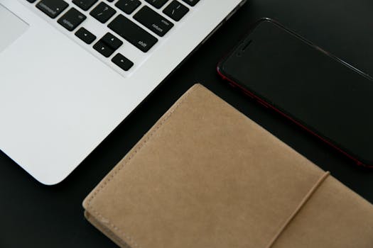 Close-up of a laptop, smartphone, and notebook on a desk, ideal for digital workspace themes.