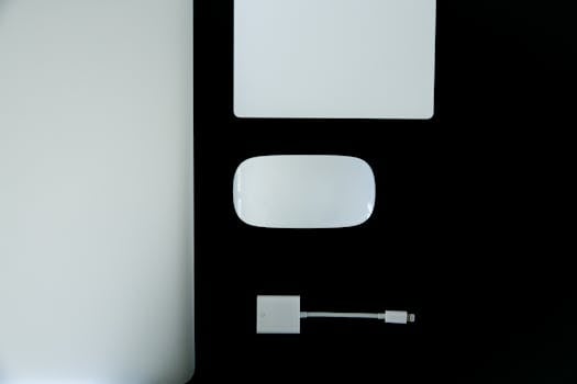 Sleek flat lay of laptop, mouse, adapter, and notebook on black and white surface.