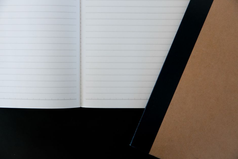 Open notebook with lined pages and cardboard cover on a black surface.