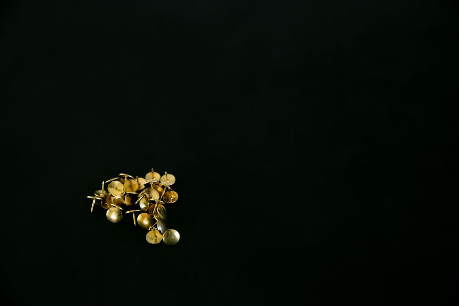 A neat arrangement of gold thumbtacks against a dark background, ideal for minimalistic designs.