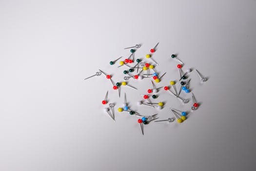 Scattered colorful push pins on a plain white surface, ideal for office and creative concepts.
