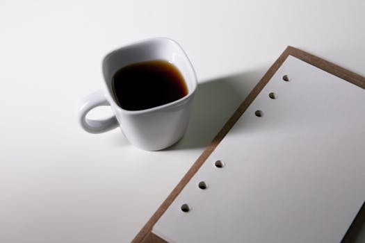 A minimalist composition features a coffee mug and notepad on a white background, perfect for productivity themes.