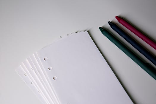 Close-up of colorful pens and white paper sheets, ideal for stationery themes.