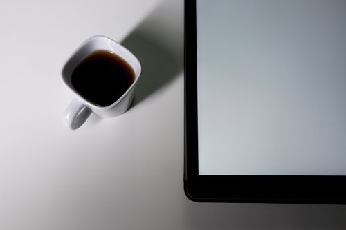 Free Minimalist top view of a coffee cup next to a tablet on a white table, offering modern simplicity. Stock Photo