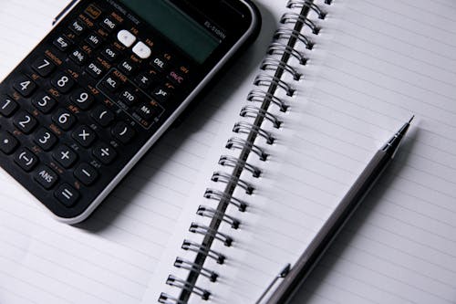 Close-up of an Open Notebook, Calculator and a Pen 