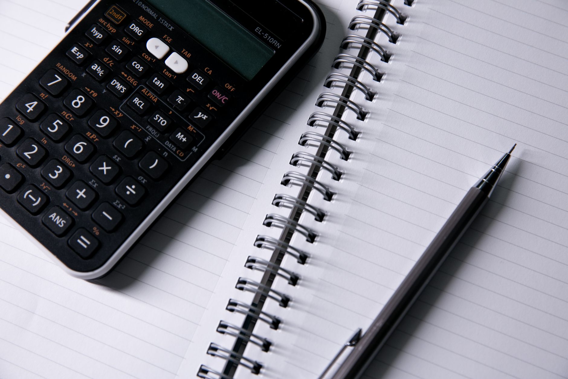 Close-up of a calculator and open notebook with a pen on a desk, ideal for office or school themes.