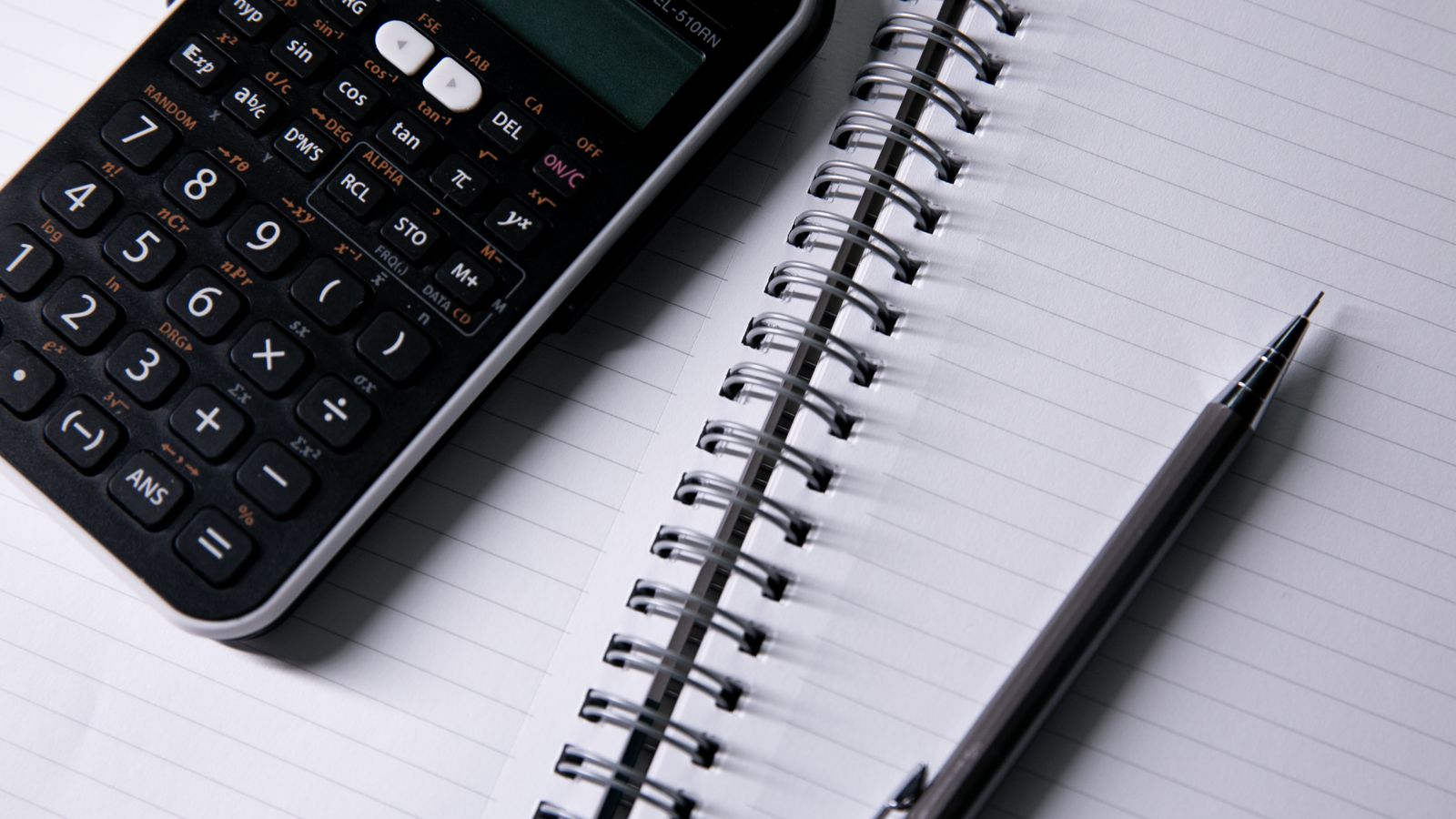A calculator and pen resting on an open lined notebook