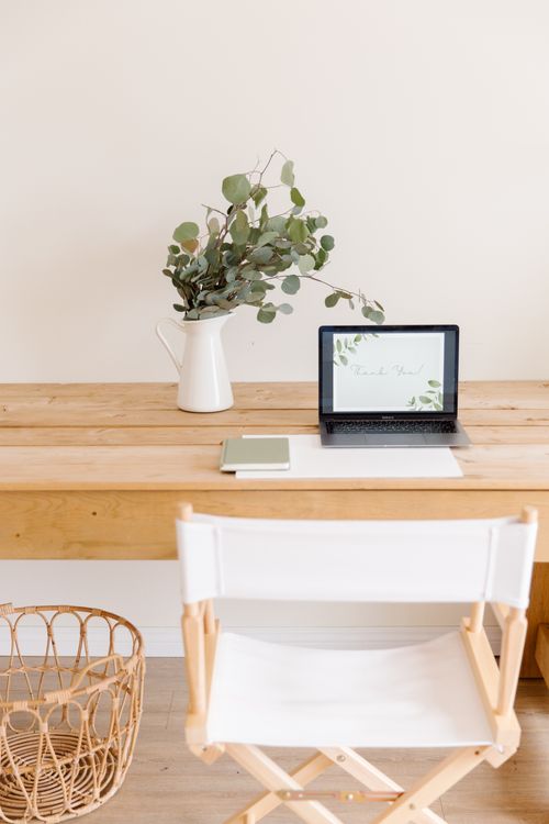 Free A clean and modern workspace featuring a laptop, chair, and eucalyptus in a vase. Stock Photo