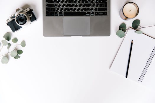 Overhead view of a minimalist workspace with a laptop, camera, candle, and notebook.