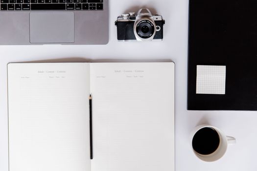 Top view of a minimalist desk setup featuring a notebook, camera, laptop, and a cup of coffee.