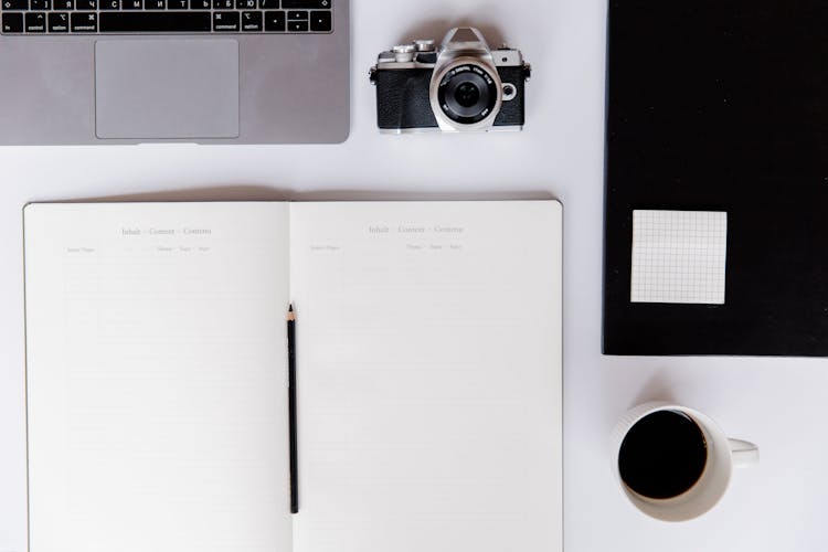 Open Notebook On Desk With Camera And Cup Of Coffee