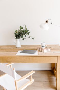 A minimalist workspace featuring a wooden desk, white chair, desk lamp, and potted plant for a serene atmosphere.