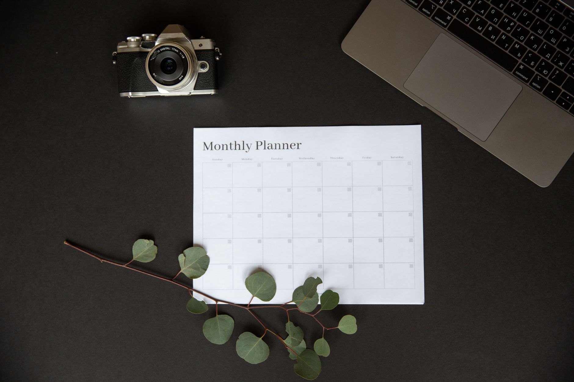 Flat lay of a monthly planner beside a camera and laptop for productivity.