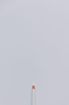 A minimalist photograph of a single white pencil with a red tip on a stark white background.