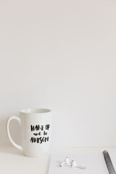 A minimalist office scene with a motivational mug, earbuds, and notebook.