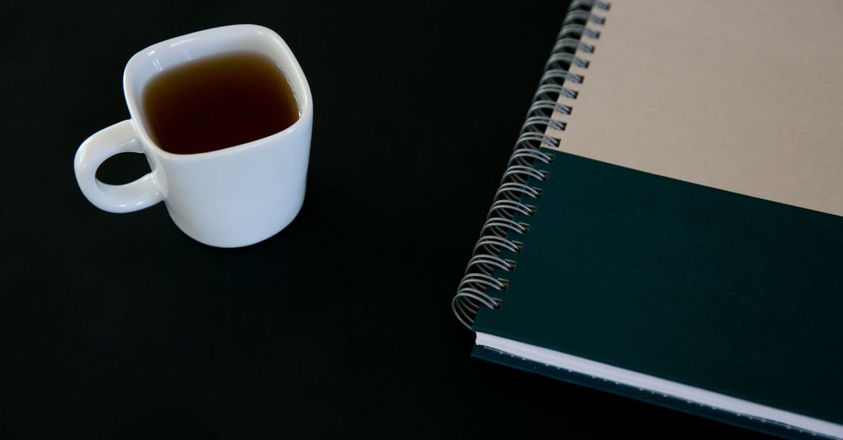 minimalist desk with closed laptop, analog notebook, and a cup of tea, soft morning light