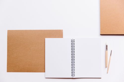 Free A simple and clean flat lay featuring an open notebook, cardboard sheets, and brushes against a white background. Stock Photo