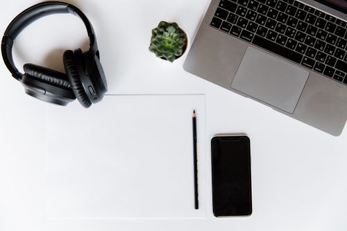 Free Top view of a modern workspace featuring a laptop, smartphone, headphones, and a pencil. Stock Photo