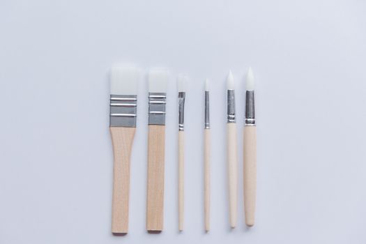A collection of six paint brushes arranged neatly on a white surface.