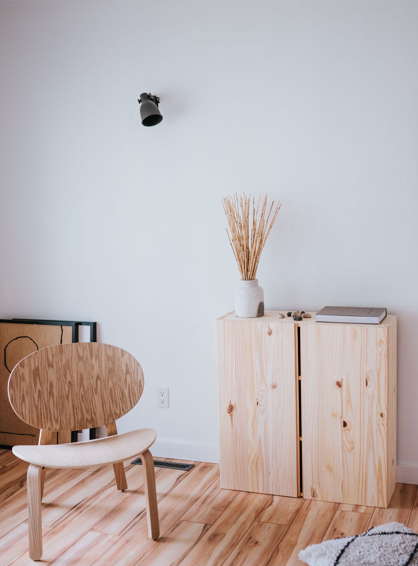 Pale timber cabinet, plywood chair and dried grasses against a white wall
