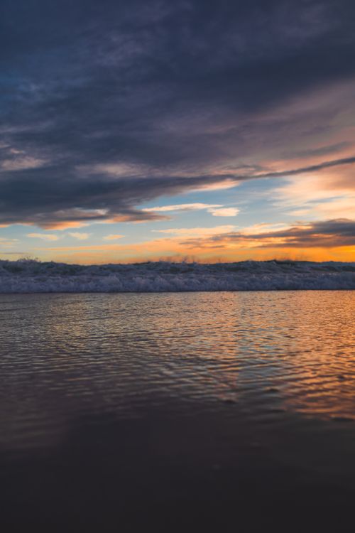 Free Captivating sunset at Arraial do Cabo with waves crashing onto the shore and a colorful sky. Stock Photo