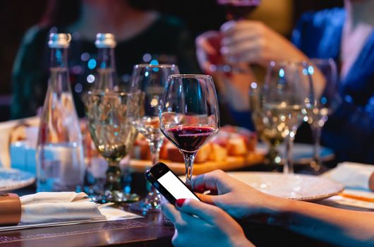 Close-up of a dinner table with wine glasses and smartphones in use, capturing modern social dining.