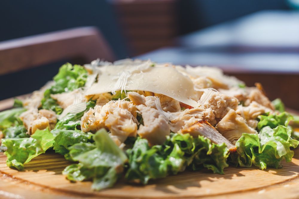 Close-up of a caesar salad with chicken and shaved cheese — Julia Filirovska on Pexels