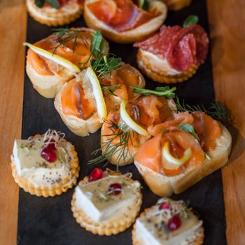A selection of canapés featuring salmon, cheese, and salami on a rustic board.