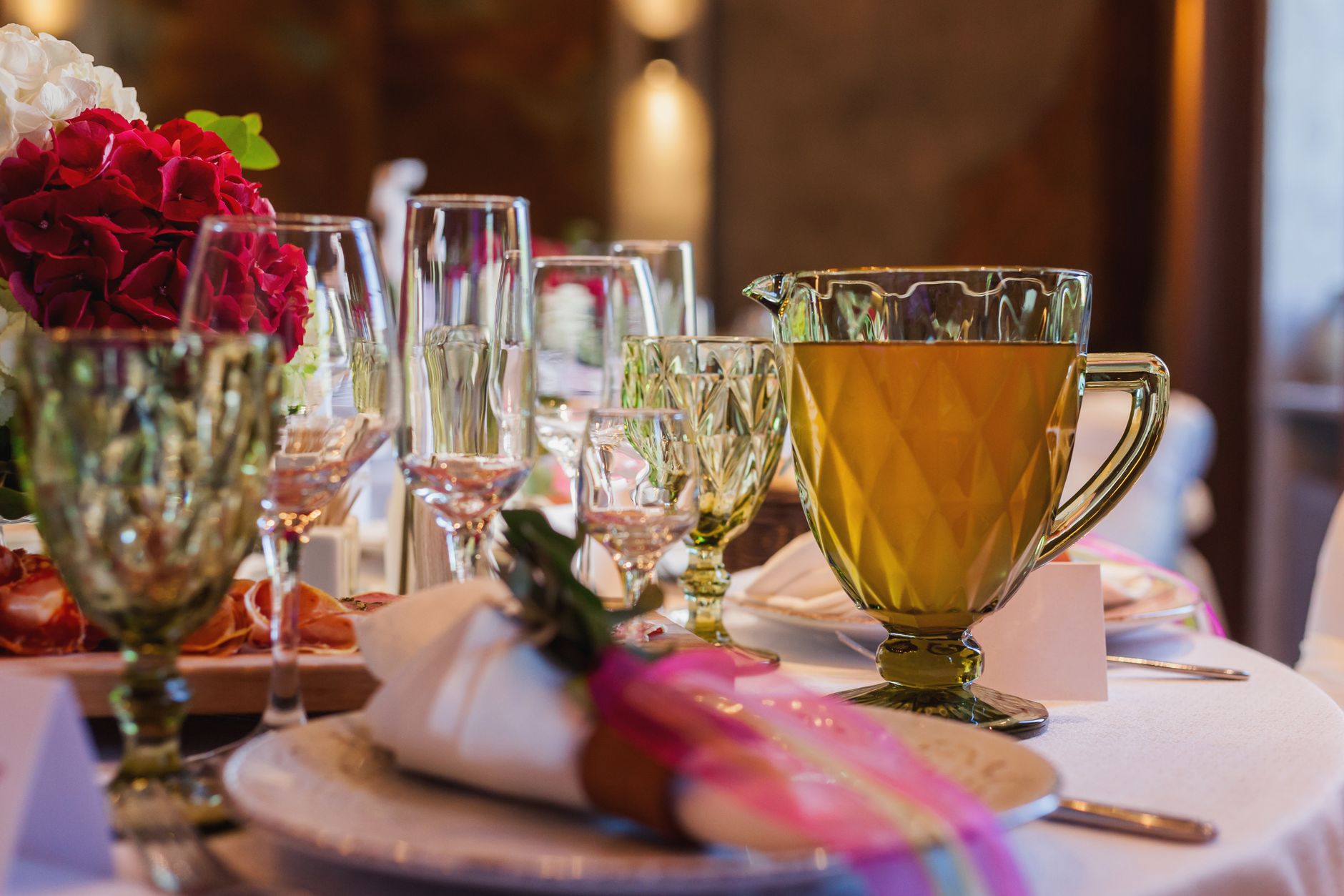 Luxurious table setting with green glassware, flowers, and elegant dishware creating an upscale dining atmosphere.