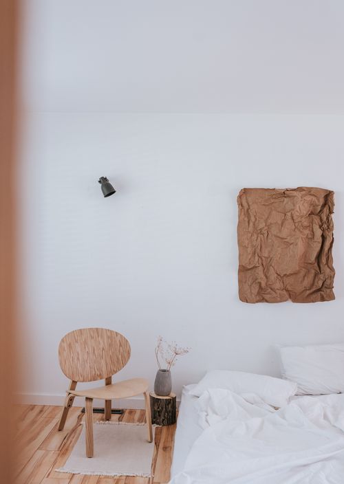 Free A minimalist bedroom featuring a wooden chair and rustic wall decor with soft natural light. Stock Photo
