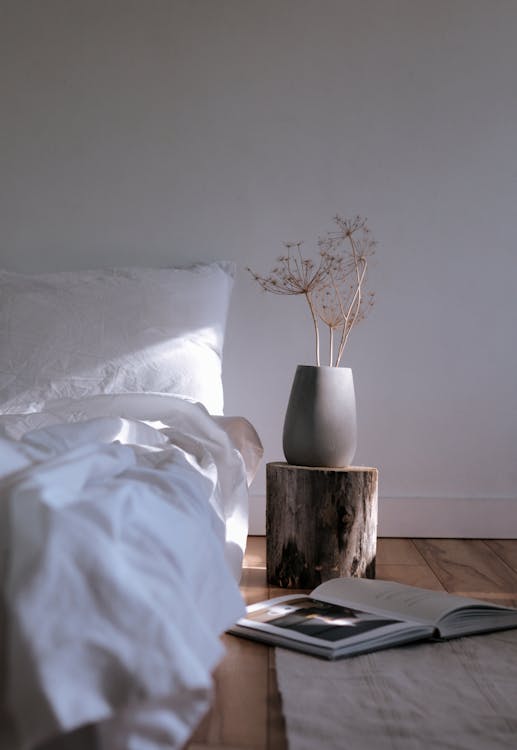 Free A White Bed with Linen Near the Chopped Wood with Ceramic Vase on Top Stock Photo