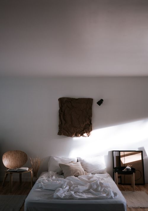 Free A minimalist bedroom featuring a bed, wooden chair, and modern art with natural light. Stock Photo