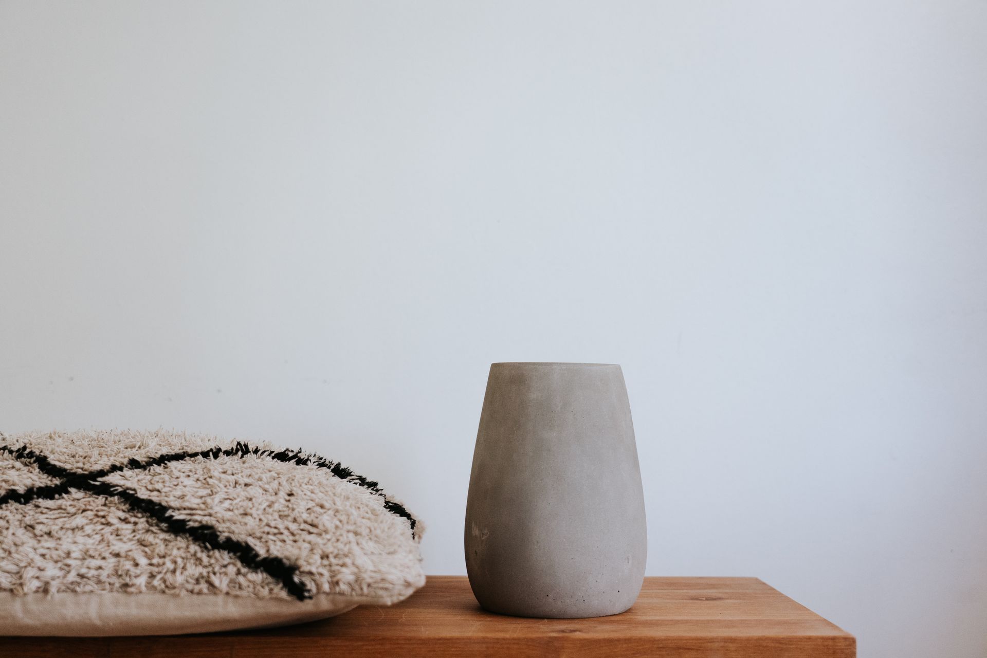 Ceramic vase and cushion on a wooden shelf in minimalist design.