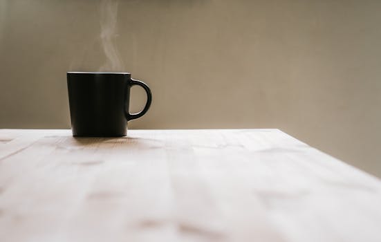 A black mug with steaming hot beverage on a wooden table. Minimalist and cozy indoor setting.