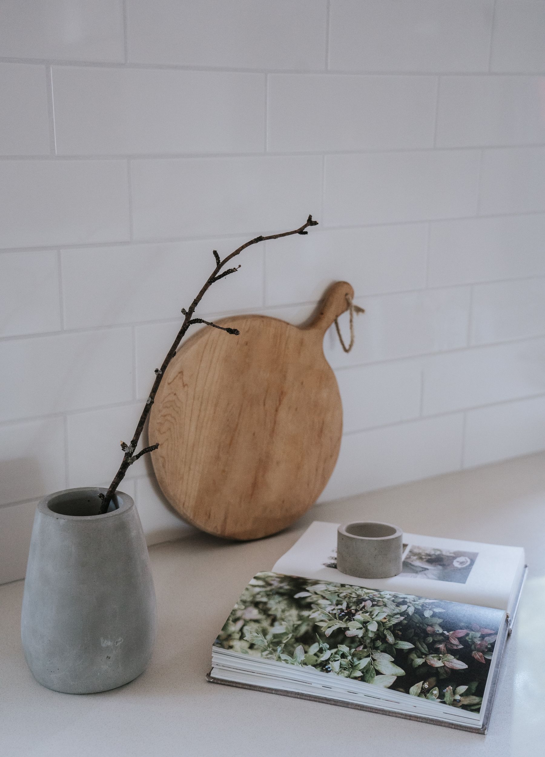 Grey vessel and cup beside a wooden chopping board on a pale work surface