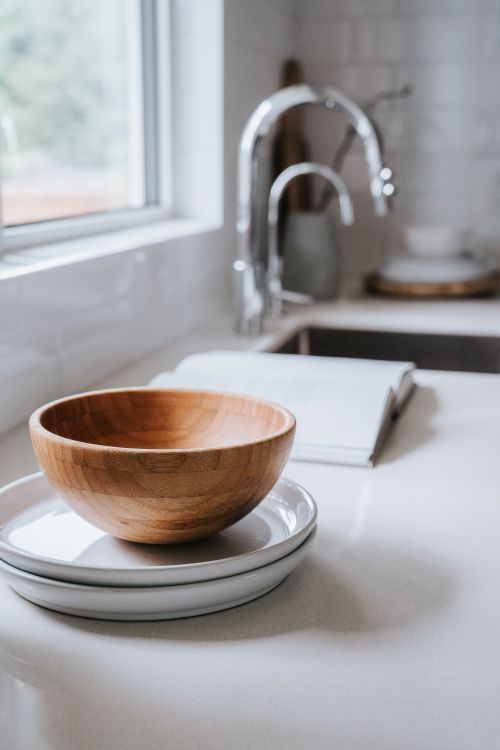 Free Stylish kitchen featuring a wooden bowl on ceramic plates and an open book by the window. Stock Photo
