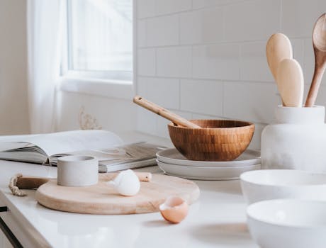 A serene minimalist kitchen setup featuring wooden bowls, spoons, and ceramic ware on a marble surface.