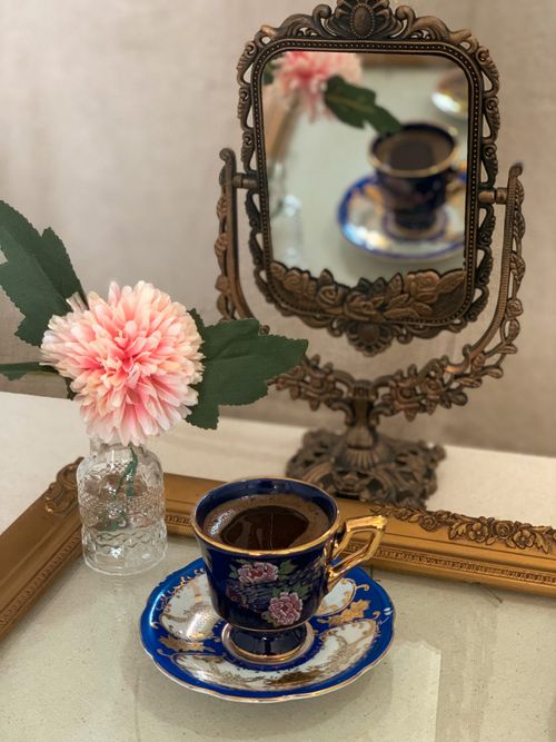 Free From above of cup of coffee and saucer placed on tray near vintage mirror and pink flower in jar Stock Photo
