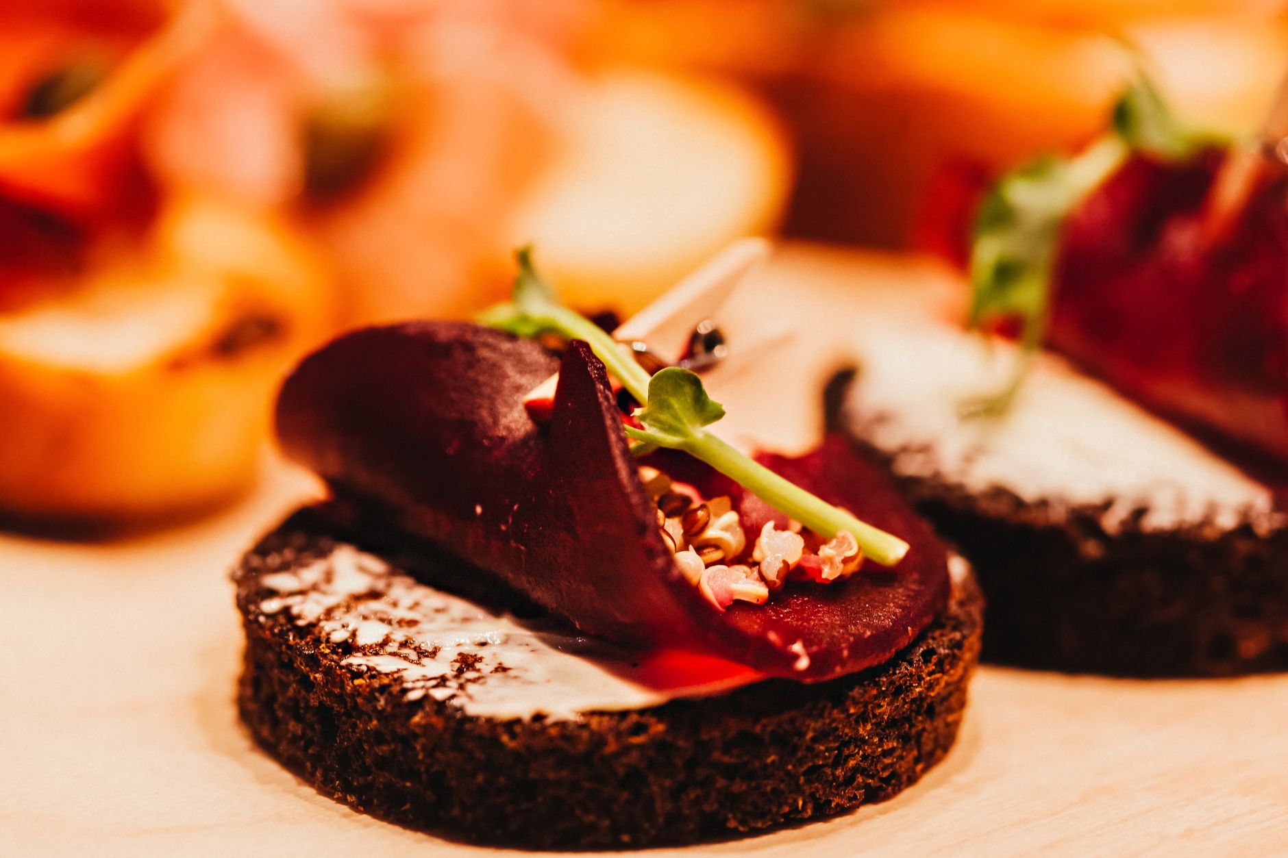Close-up of a gourmet canapé featuring beetroot, quinoa, and greens on rye bread.